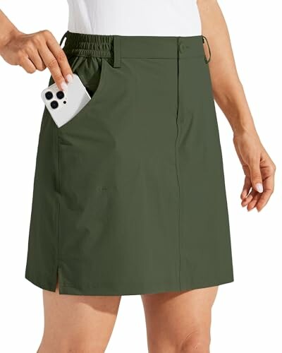 Person placing phone in pocket of green skirt.
