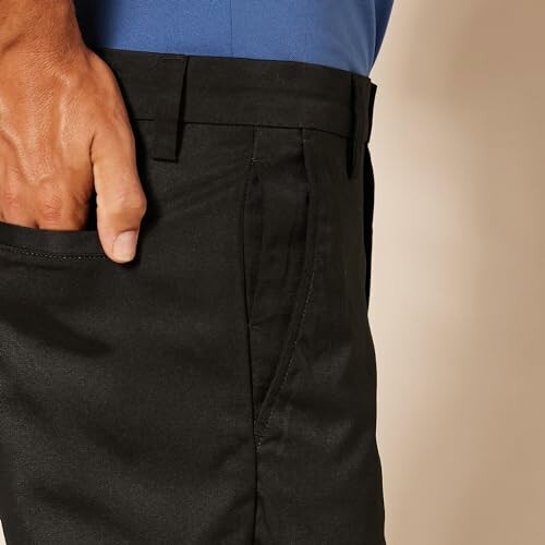 Close-up of a man wearing black pants and a blue shirt with one hand in the pocket.